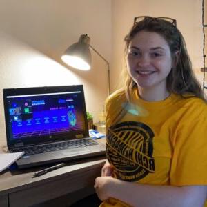 smiling student sitting at a desk while attending a virtual conference for Phi Theta Kappa